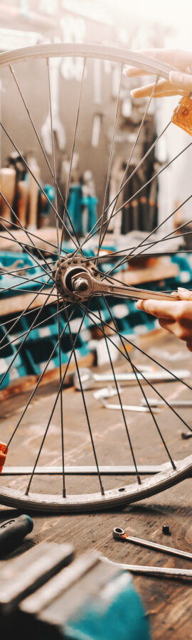 Cute Caucasian female worker holding and repairing bicycle wheel while standing in bicycle workshop.