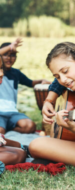 Shot of a group of teenagers playing musical instruments in nature at summer camp