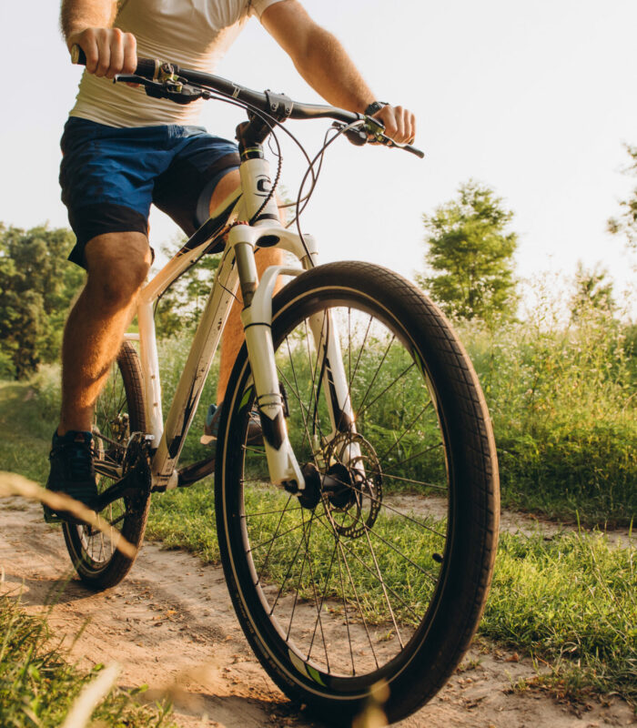 A man rides a bicycle on a dirt road in the summer at sunset. Active rest in the summer on bicycles. Cycling between the fields in the summer at sunset.